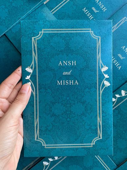 Holding one of the teal invitation folders. The color is bold and unique, making a memorable first impression for the wedding guests.