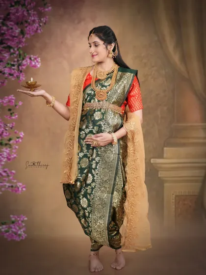 A stunning portrait of a mother-to-be in a traditionally draped green saree, holding a diya. The pose and lighting evoke a sense of divinity and grace, celebrating the light of new life.