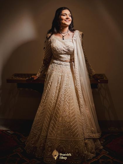 A full-length portrait of the bride in her elegant white sangeet lehenga. The soft lighting highlights the intricate details of her outfit and her radiant smile.