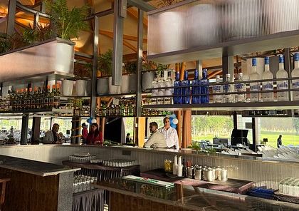 A view from behind the bar at KGA, looking out onto the golf course. The indoor landscaping is designed to frame the view, seamlessly connecting the interior space with the vast green landscape outside.