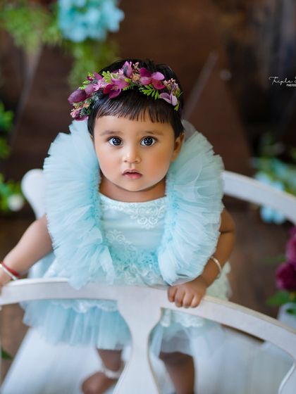 A stunning close-up portrait of a baby girl with a floral headband. Her direct gaze and beautiful eyes are the centerpiece of this simple and elegant shot.