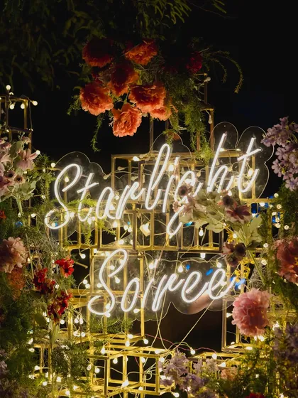 A custom neon sign reading "Starlit Soiree," nestled within a golden structure and surrounded by florals, creating a perfect, instagrammable branding moment for the event.