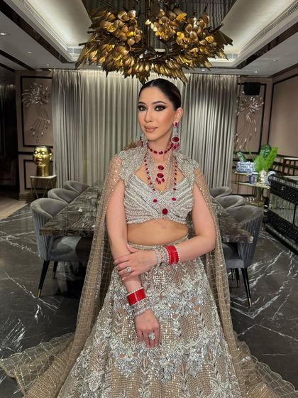A frontal view showcasing the stunning ruby jewelry against the silver and gold lehenga. The makeup is warm and defined, with a focus on the eyes.