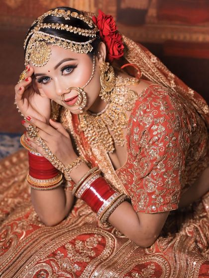 A bride lying down in a beautiful red and gold lehenga, a classic pose for bridal photography.