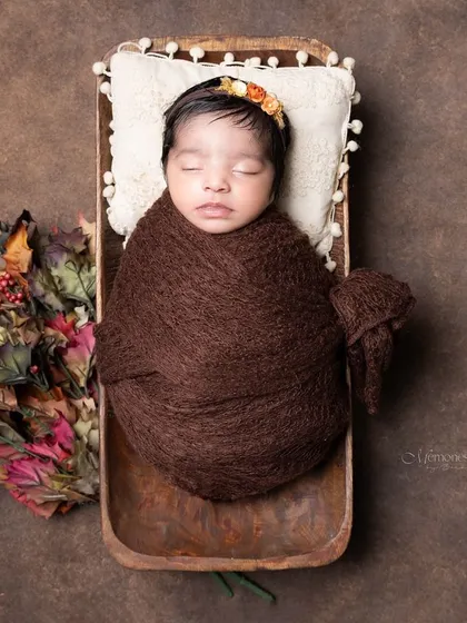 An earthy, autumn-toned newborn portrait. The rich brown wrap and fall leaves create a warm and cozy feel.
