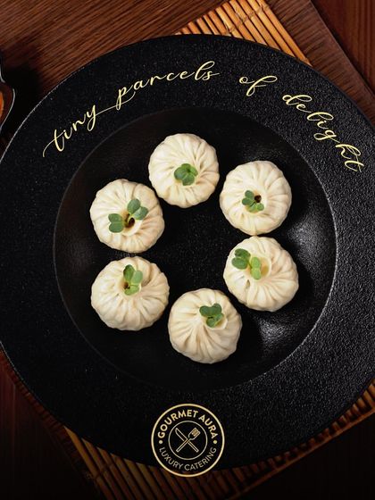 "Tiny parcels of delight." Six perfectly formed dumplings are presented on a textured black plate, showcasing the meticulous craft that goes into each bite-sized creation.