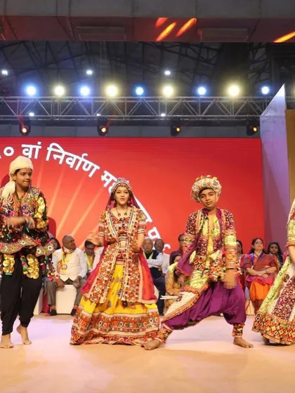 A troupe of folk dancers in vibrant traditional attire performing on stage for the Lord Mahavir foundation day event. We provide authentic cultural performers for religious festivals and community celebrations.