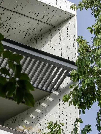 A detail of the perforated facade seen through trees, showcasing the beautiful interplay between the man-made structure and the natural environment.