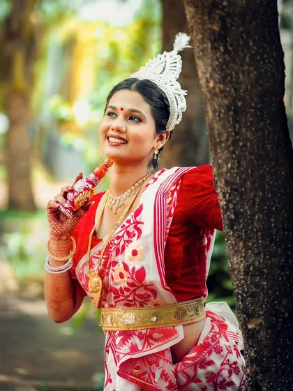 A happy and radiant portrait of the bride, holding a traditional Bengali wedding accessory and smiling brightly.