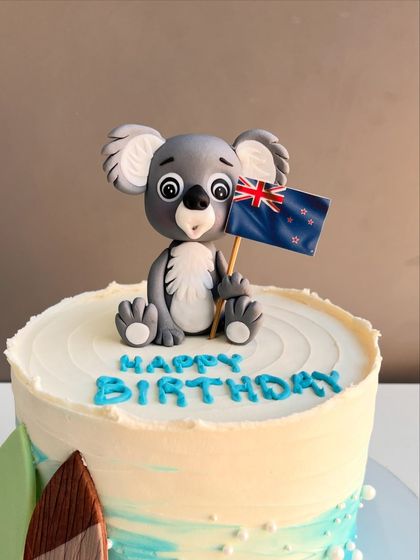 A close-up of the adorable, hand-sculpted koala topper, showing the detailed texture and the tiny New Zealand flag it's holding.