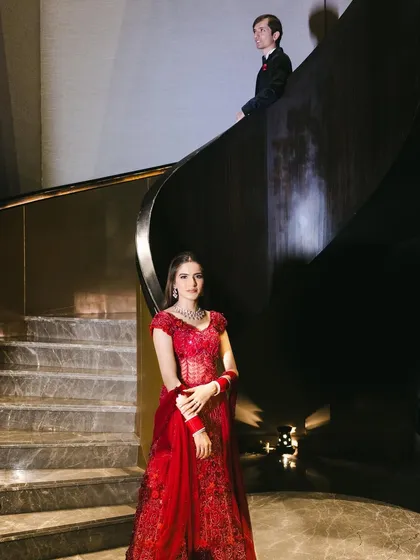 An artistic shot capturing the bride and groom. Her glamorous red look stands out, creating a cinematic and romantic wedding portrait.