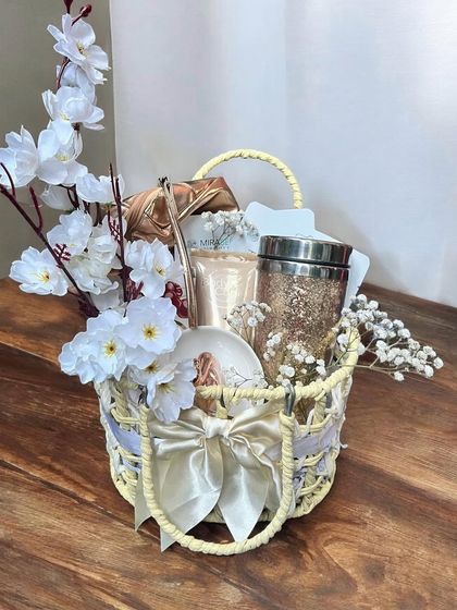 An elegant and serene gift basket for her in a white and gold theme. It features a glittery tumbler, a decorative plate, and other items, accented with delicate white flowers.