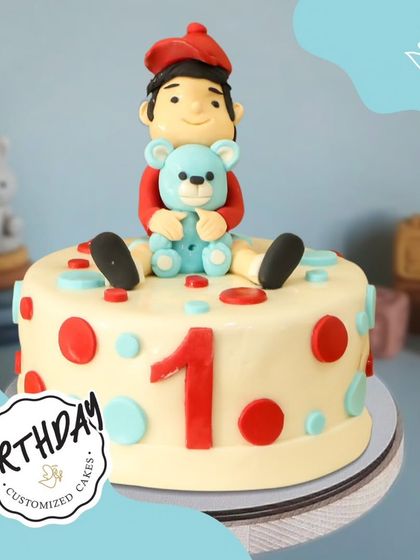 A cute and colorful cake for a first birthday, featuring a little boy holding his favorite teddy bear. The polka dots add a playful touch.