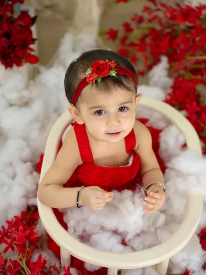 A sweet, direct-to-camera look from a little girl in a red dress, surrounded by fluffy clouds.