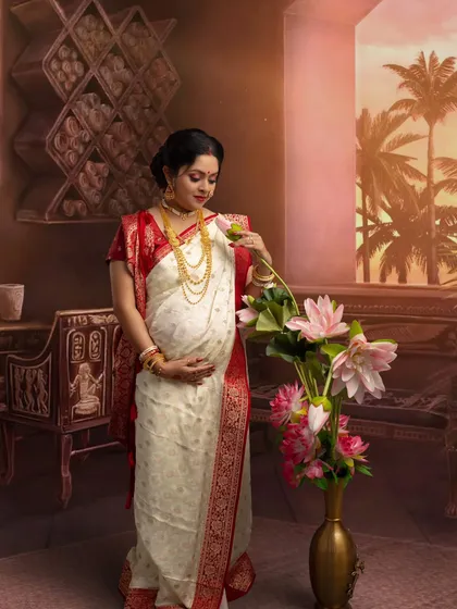 A quiet moment of reflection. The mother-to-be, dressed in a beautiful Bengali saree, arranges lotus flowers, symbolizing purity and divinity in a classic, vintage setting.