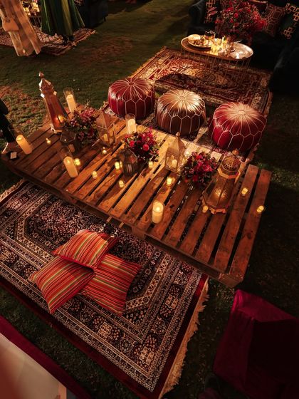 A full view of the picnic seating, with layered rugs, cushions, and ottomans creating a relaxed and bohemian vibe. The candlelight makes the space feel incredibly warm and intimate.