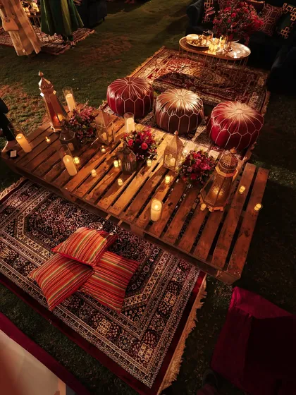 A full view of the picnic seating, with layered rugs, cushions, and ottomans creating a relaxed and bohemian vibe. The candlelight makes the space feel incredibly warm and intimate.