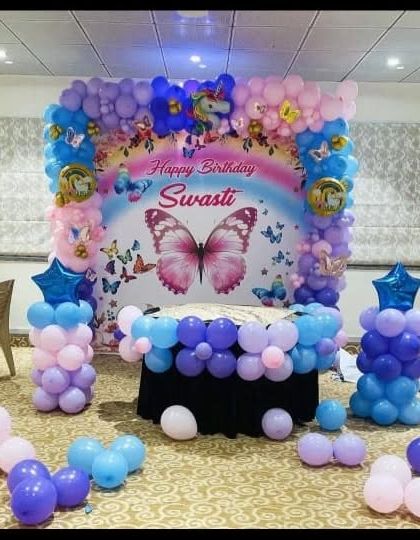 A butterfly and rainbow themed backdrop with a balloon arch in pastel colors.