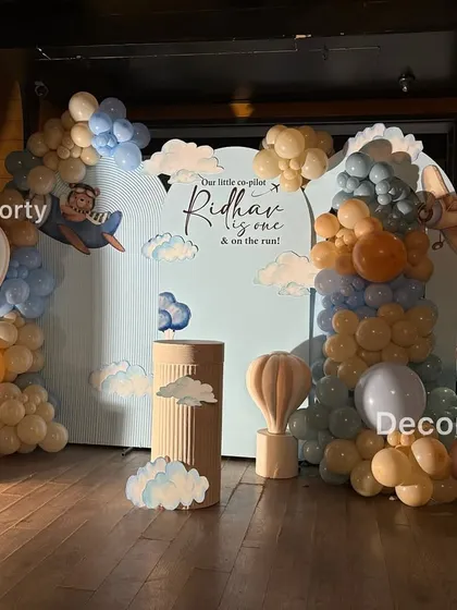 For the little pilot's first flight, this "Urso Aviador" or Aviator Bear theme is perfect. The setup features a personalized backdrop, a large light-up number one, and adorable teddy bear and hot air balloon props.
