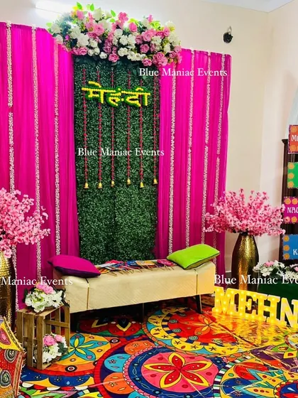 A funky and colorful Mehendi setup. This design uses a vibrant printed carpet, a green backdrop with a 'Mehendi' sign, marquee letters, and fun props, creating a lively and playful atmosphere.