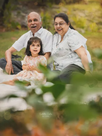 A happy family moment with grandparents and their granddaughter enjoying a picnic in the park. The genuine smiles show the warmth and love shared between them.