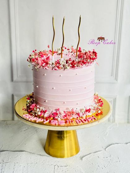 Soft hues, delicate blooms, and a golden glow. This pretty pink cake is adorned with a wreath of dried flowers and tall, elegant candles.