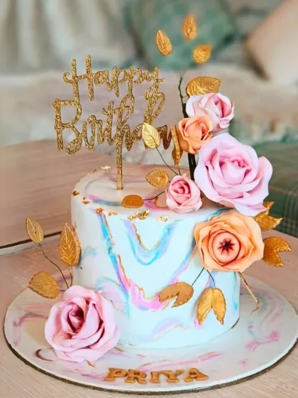 A beautiful cake with a soft blue and pink marble finish, decorated with a cascade of sugar roses and gold-painted leaves.