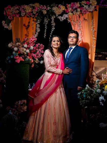 A full-length portrait of the couple at their sangeet or engagement, framed by beautiful floral decor.