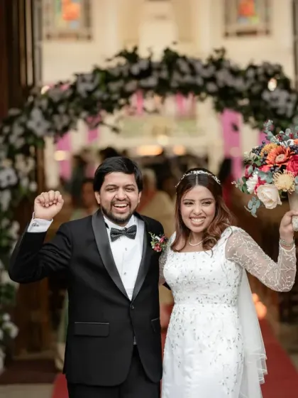 Just married! The couple exits the church with triumphant smiles and hands raised in joy. This photo captures the pure elation of starting their new life together after a beautiful Christian wedding ceremony.