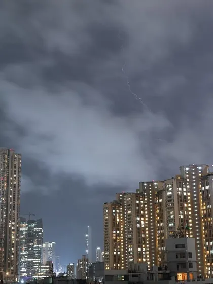 A lightning bolt strikes down behind a tall residential building in Mumbai during a thunderstorm.