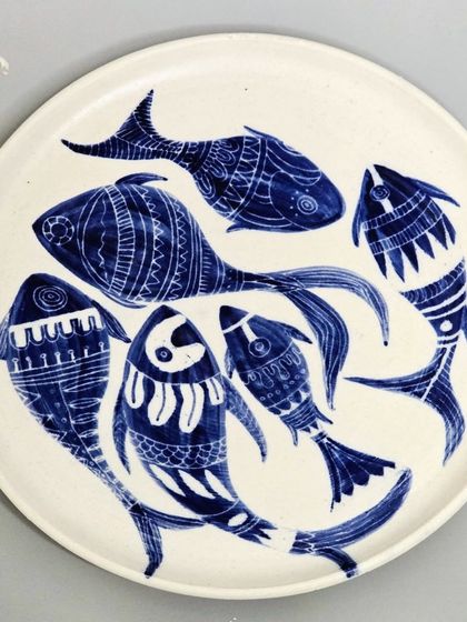 A top-down view of a hand-painted ceramic plate, showcasing a dynamic composition of fish. Each piece is meticulously crafted to be a unique work of art for your home.