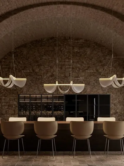 A row of Drape Lights by Jamie Wolfond for Moooi illuminates a long dining table in a rustic, vaulted cellar. The design, like a perfectly draped fabric, brings effortless grace and warmth.