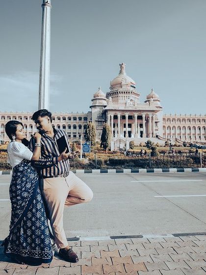 A duplicate of a grand wide shot of a couple walking hand-in-hand in front of the magnificent Vidhana Soudha.