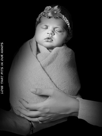 A dramatic black and white photo showing a mother's hands wrapped around her sleeping baby. The caption "Love that fits in our hands" perfectly describes this precious, tiny stage.
