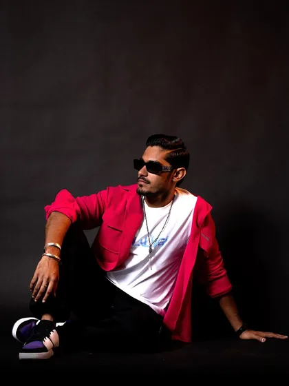 A relaxed, seated pose in the pink shirt outfit. The sunglasses add a touch of cool, completing this casual yet stylish ensemble.