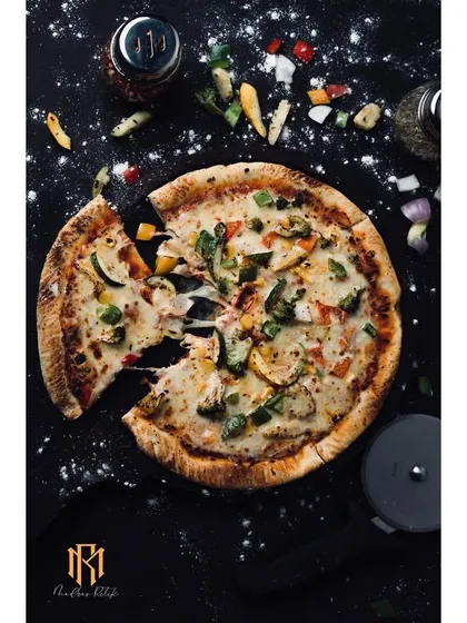 A dynamic overhead shot of a pizza, styled with scattered ingredients for an editorial feel. This dark, moody photography is perfect for restaurants wanting to create a premium, artisanal brand image.
