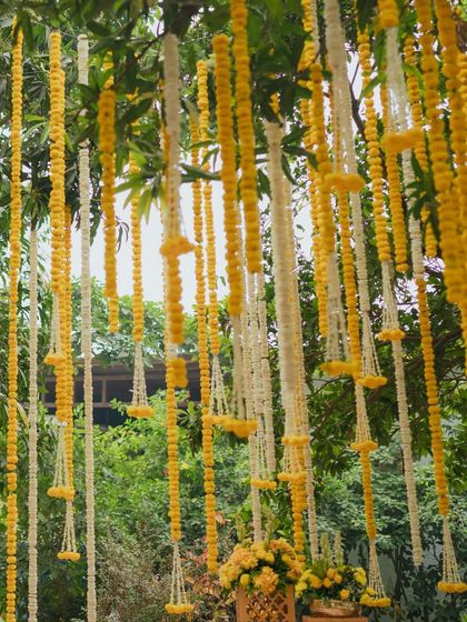A beautiful shot looking up at the canopy of hanging marigold and tuberose strings, creating a curtain of flowers against the green foliage of the trees.