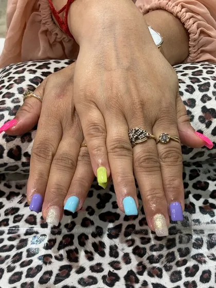 A playful and vibrant multi-color manicure. Each nail is painted with a different pastel shade, including neon yellow, lavender, and sky blue, with glitter accents for a fun and eye-catching result.