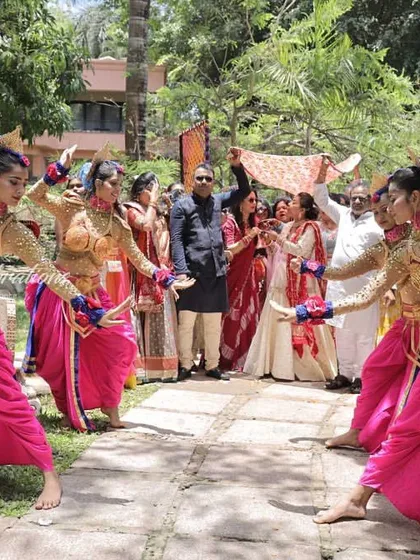 A joyous daytime function entry for the Bhaat ceremony at a Goa wedding. The traditional costumes of the dancers pop against the lush green background, creating a beautiful scene.