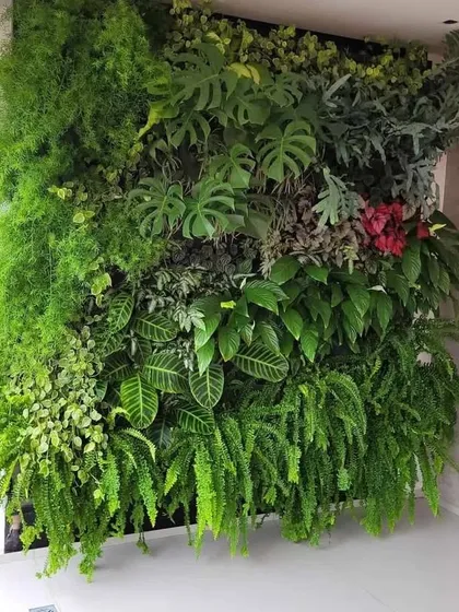 A dense and lush artificial green wall installed indoors. This floor-to-ceiling installation uses a variety of large-leaf and trailing plants to create a dramatic, jungle-like effect.