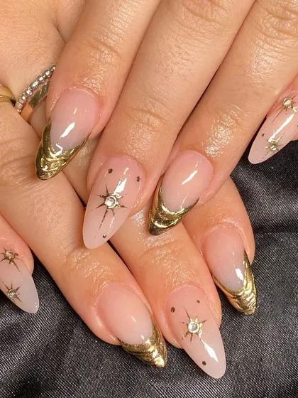 A glamorous set with a sheer nude base, metallic gold French tips, and hand-painted starburst accents.