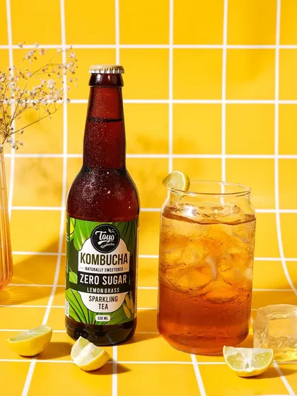 A vibrant shot using a yellow tiled background. The grid pattern adds visual interest and structure to the composition, making the kombucha bottle pop.