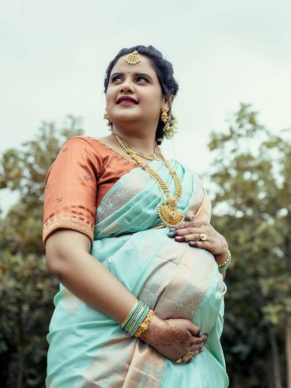 A beautiful solo portrait of a mother-to-be in a traditional light blue saree, looking up with a hopeful expression during her outdoor baby shower photoshoot.