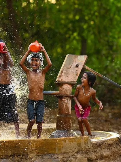 A group of boys and a girl enjoying a water fight, their expressions a mix of laughter and concentration. This image captures the dynamic interaction and shared joy of their game.