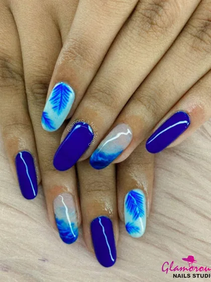 A beautiful blue-themed set combining solid royal blue nails with accent nails featuring a blue ombré and a delicate feather-like design.