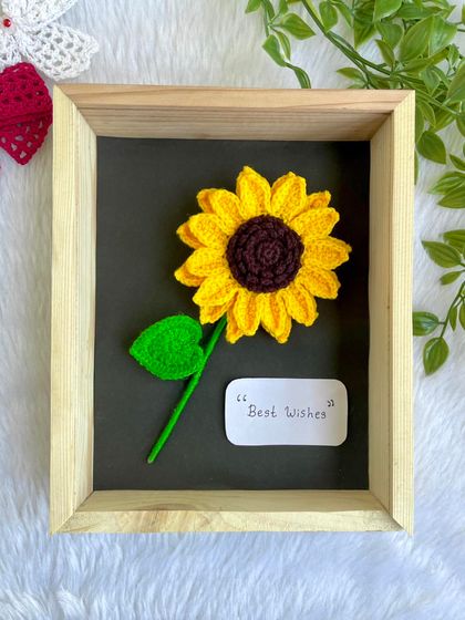 A single, large crochet sunflower beautifully displayed in a wooden frame with a "Best Wishes" note. It makes for a thoughtful and unique gift.