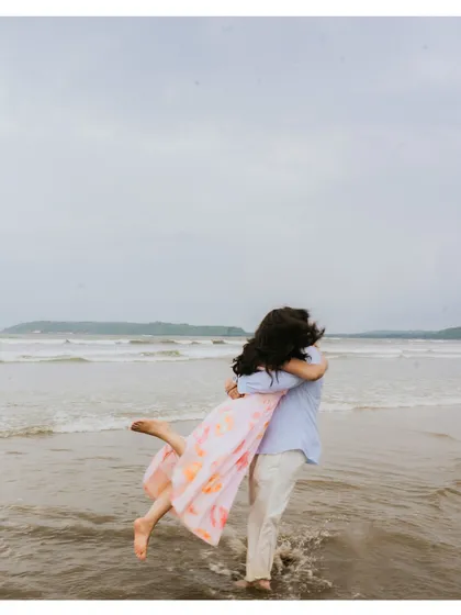 A playful and romantic moment from a beach pre-wedding shoot, with the groom lifting his bride in the shallow water.