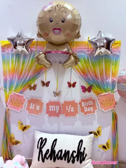 A close-up of the half-birthday backdrop, showing the colorful tassel curtain, butterfly details, and the personalized 'Rehanshi' cushion.