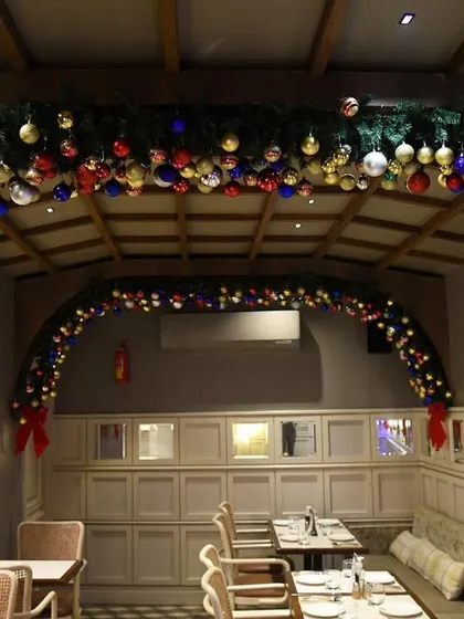 Traditional Christmas decor for a restaurant, with lush green garlands studded with colorful ornaments, arching over the dining booths.