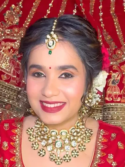A close-up portrait against a richly embroidered background. The bride's makeup is classic and elegant, a perfect match for her traditional red and gold lehenga.